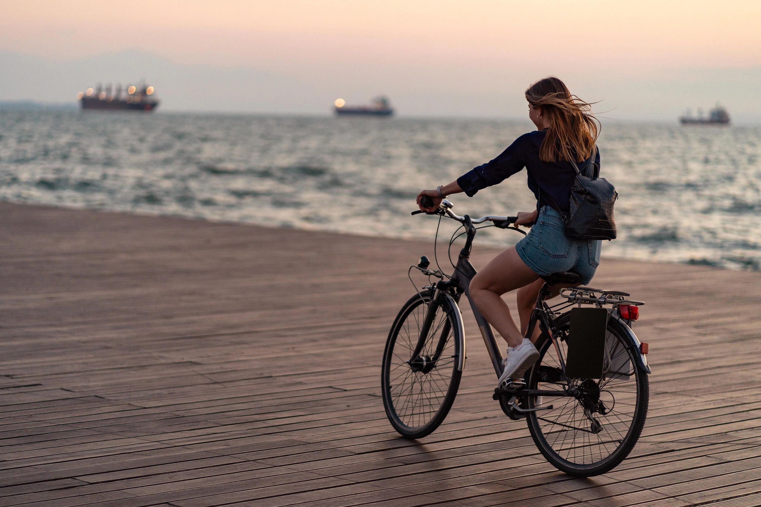 Woman riding a bike by the sea at dusk