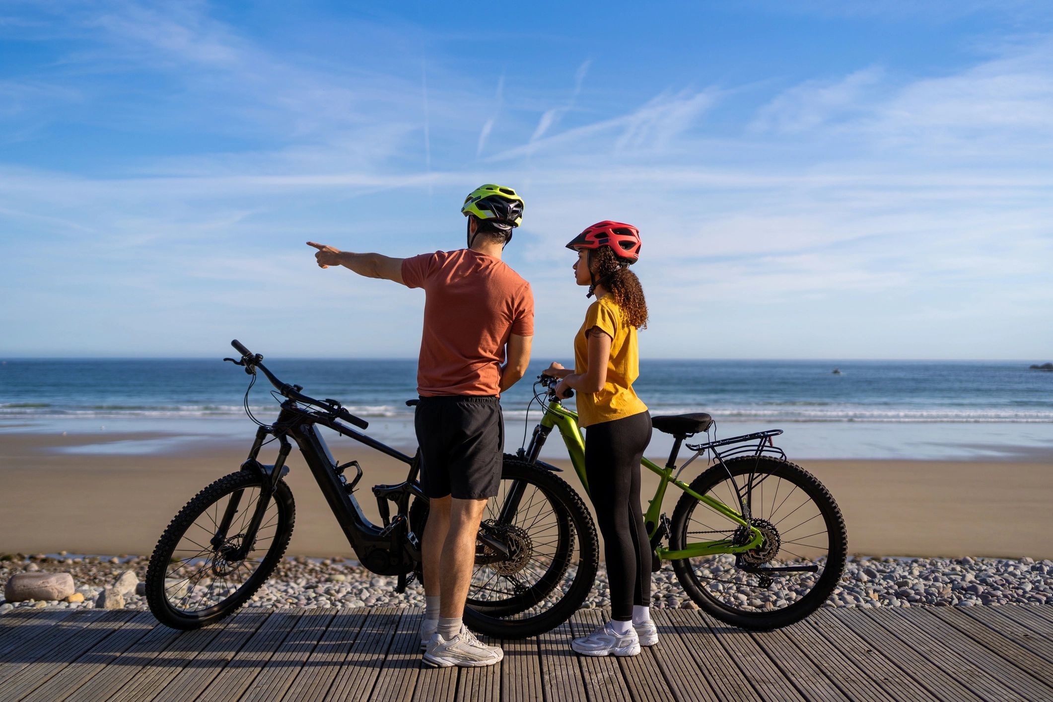 Two people with e-bikes on a beach boardwalk looking out at the ocean